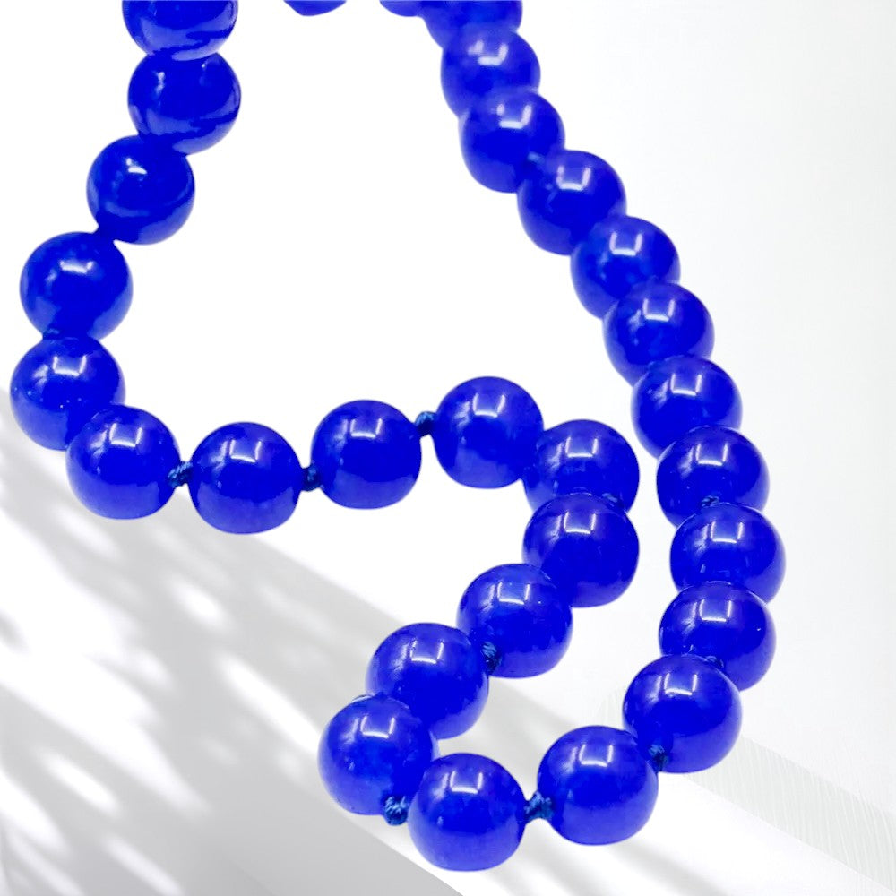 A strand of glossy, polished cobalt blue beads arranged in a curved loop on a clean white background.