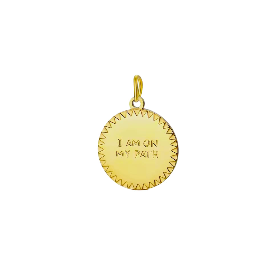 Gold pendant with 'I am on my path' engraving on a light gray background