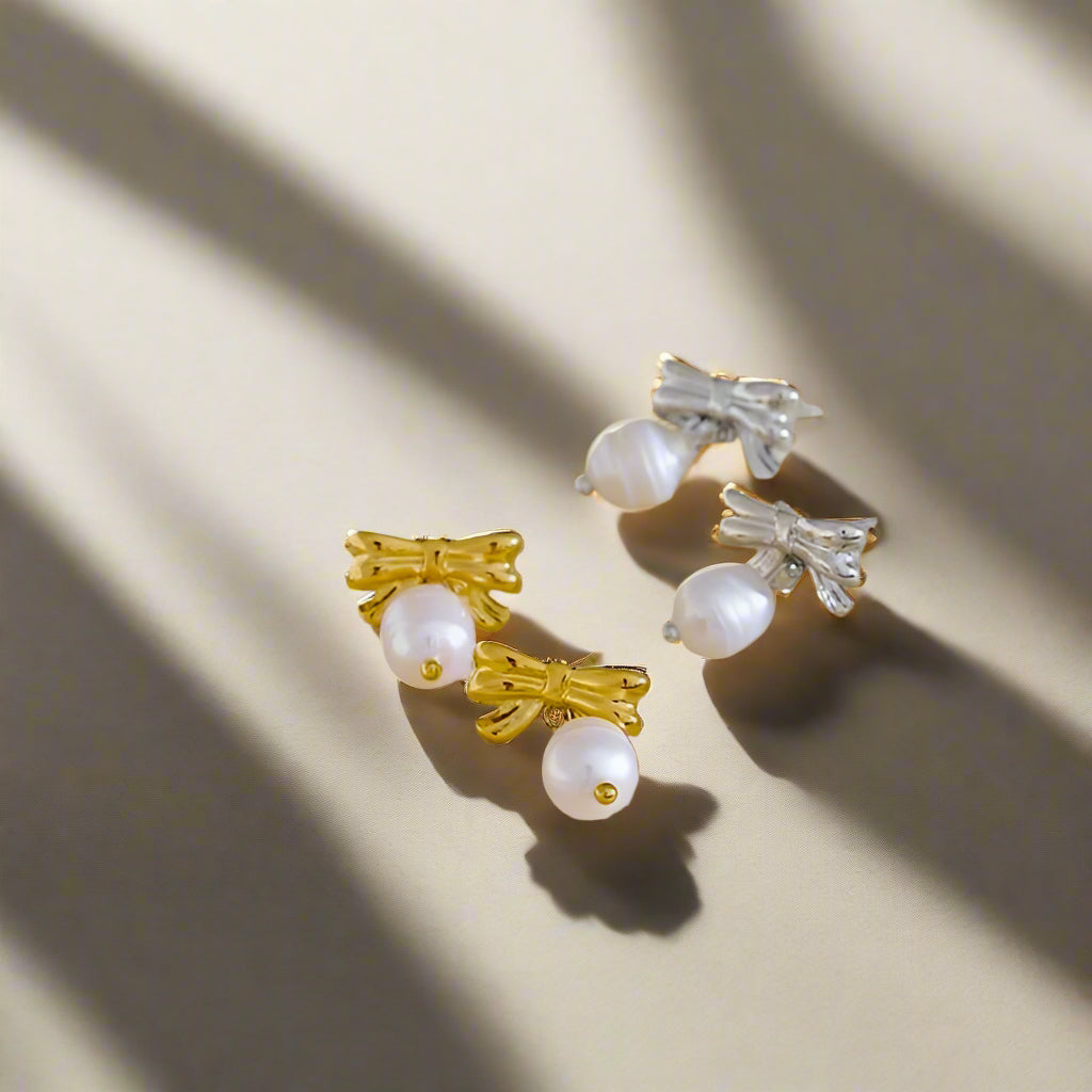 Pair of earrings with gold bows and pearls on a beige background
