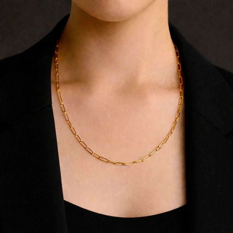 Gold chain necklace on a women wearing a black outfit against a dark background