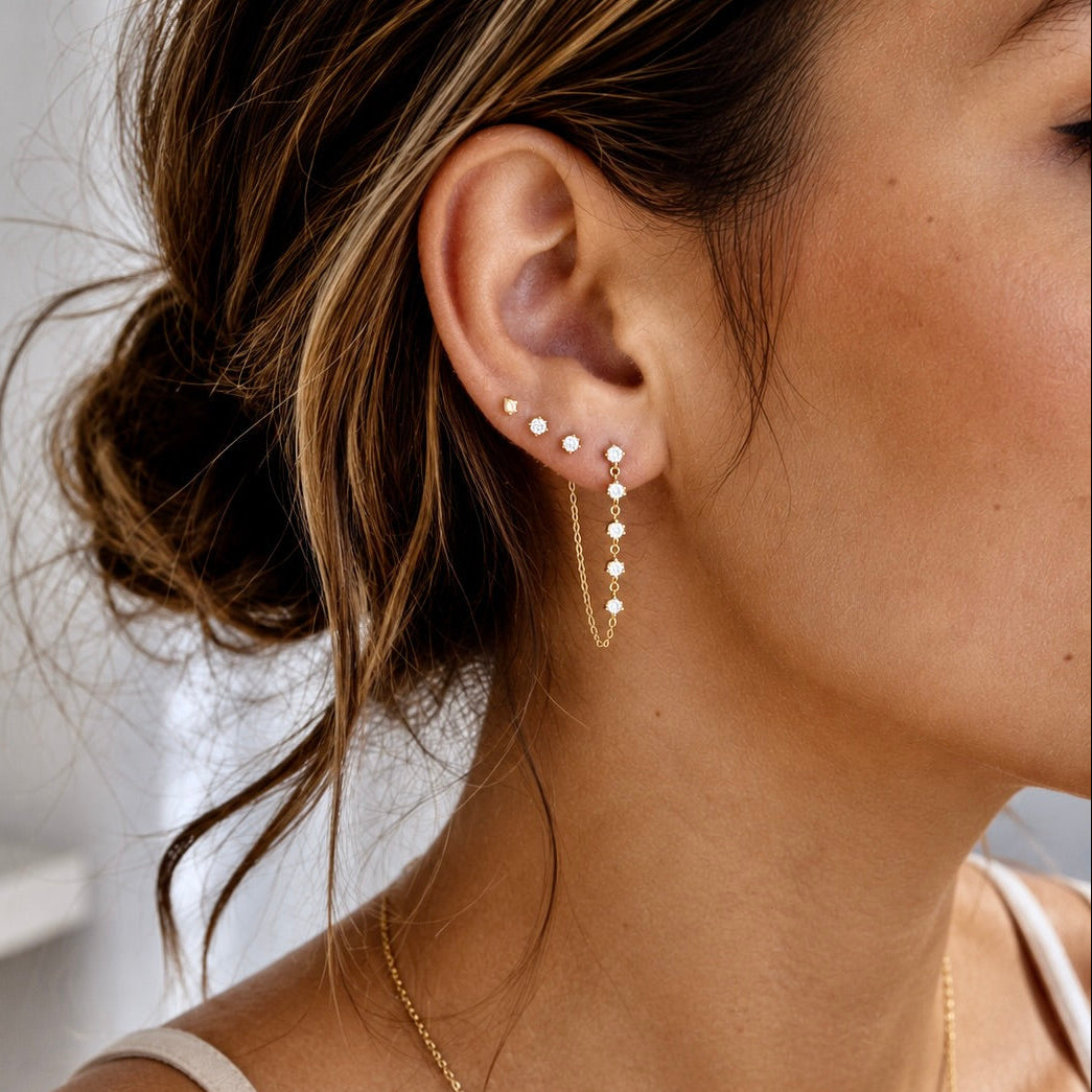 A close-up lifestyle shot of a woman wearing a delicate gold ear cuff with multiple small pearl-like studs and a matching drop earring with a chain and pearl-like beads.