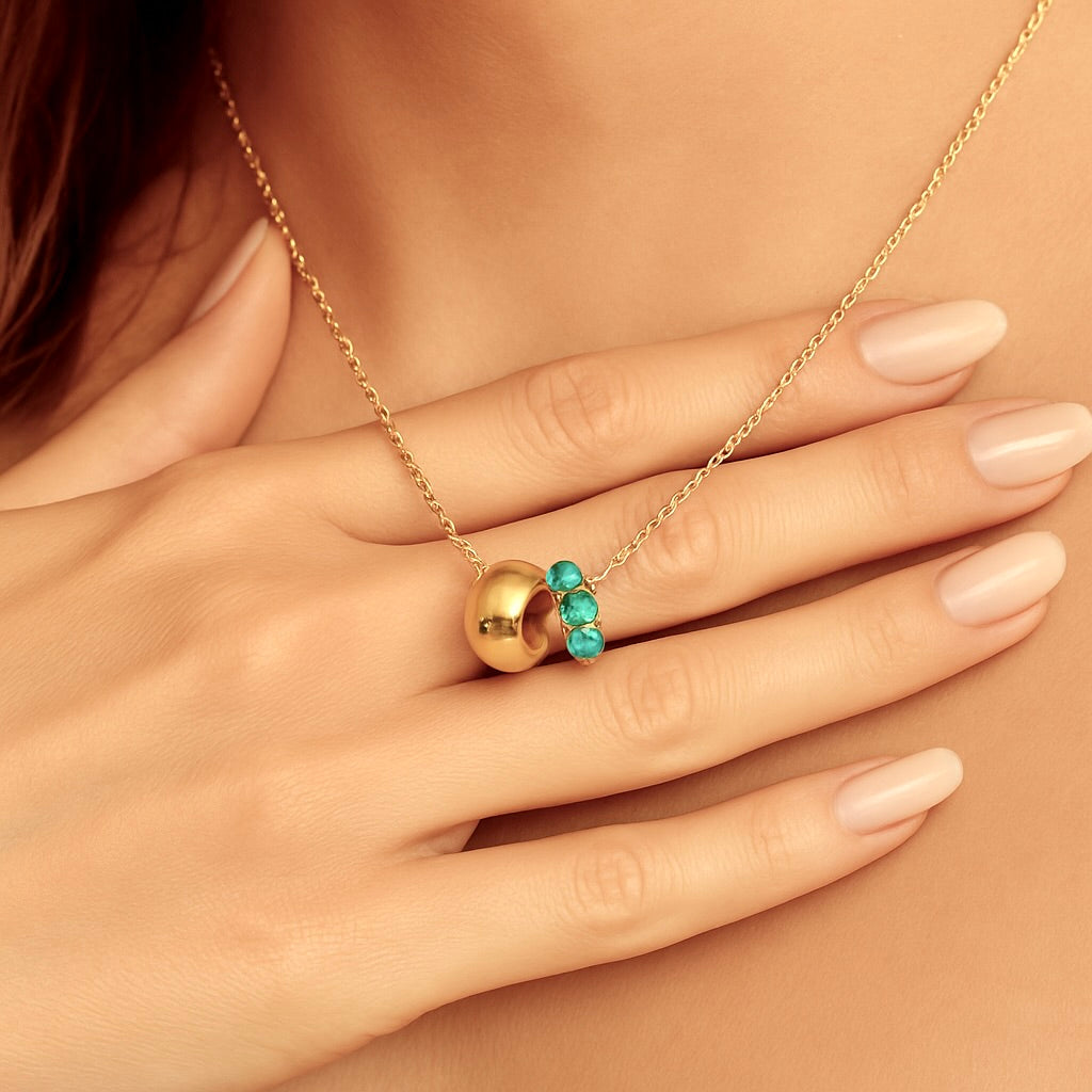Gold necklace with turquoise stones held by a hand on a beige background