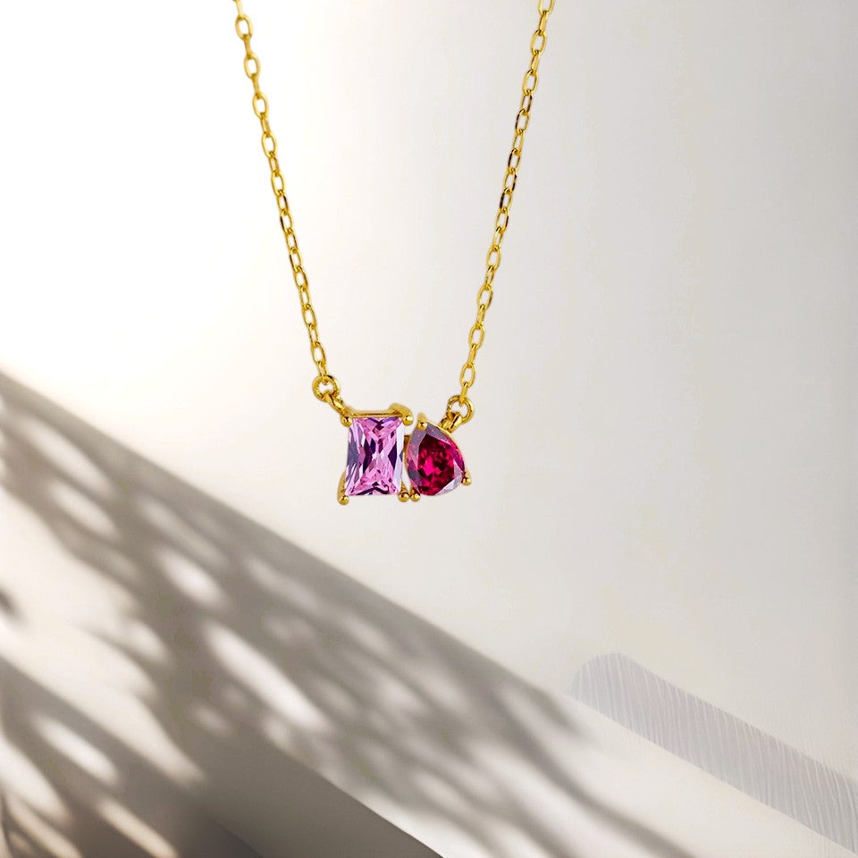 Gold necklace with two colorful gemstones on a light background