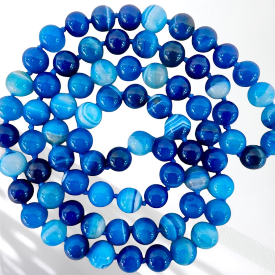 A coiled strand of round blue agate beads in various shades of royal, navy, and light blue with white banding, displayed on a clean white background.