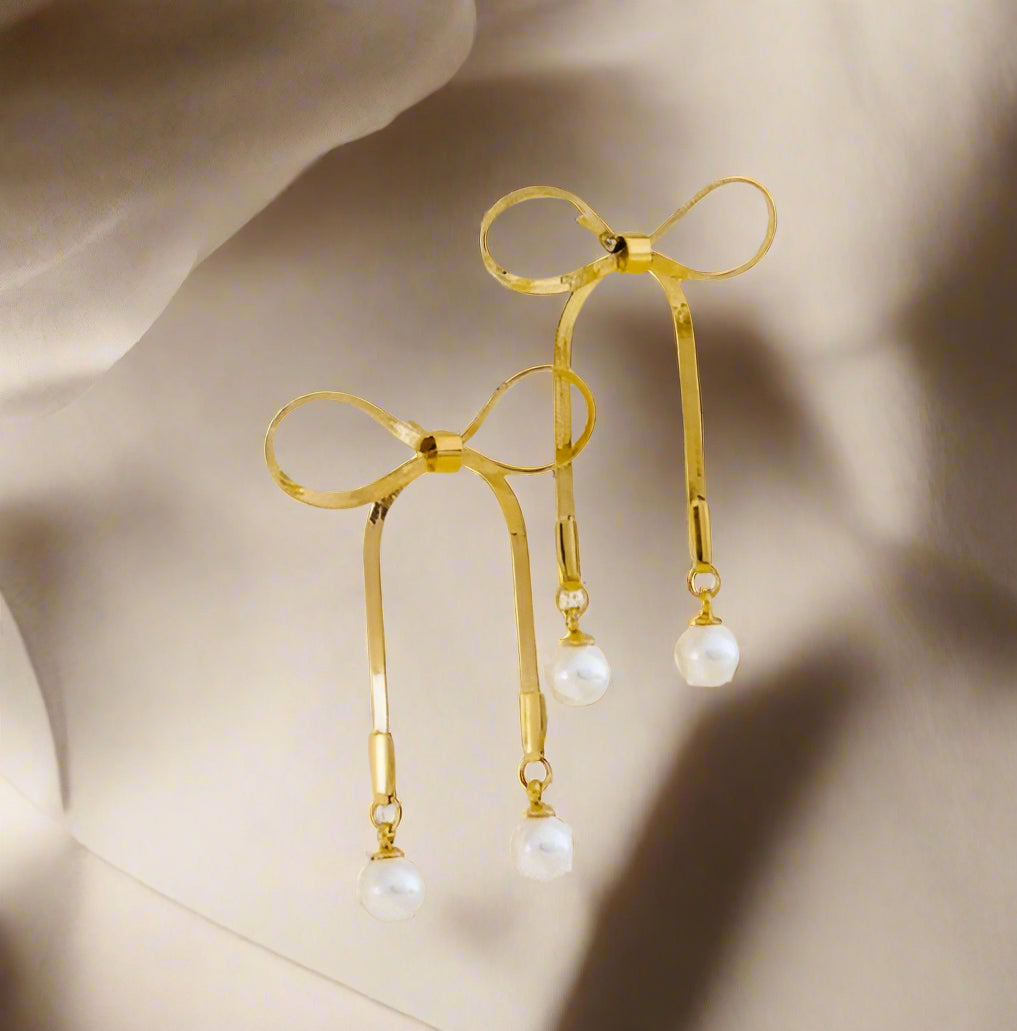 Gold earrings with pearl drops on a textured beige surface