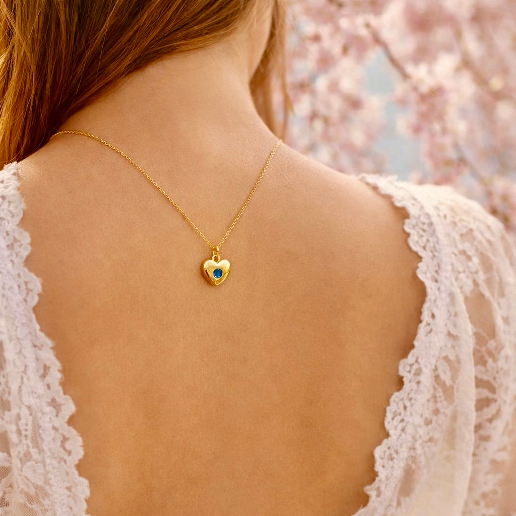 Gold necklace with a heart-shaped pendant worn by a person against a cherry blossom background