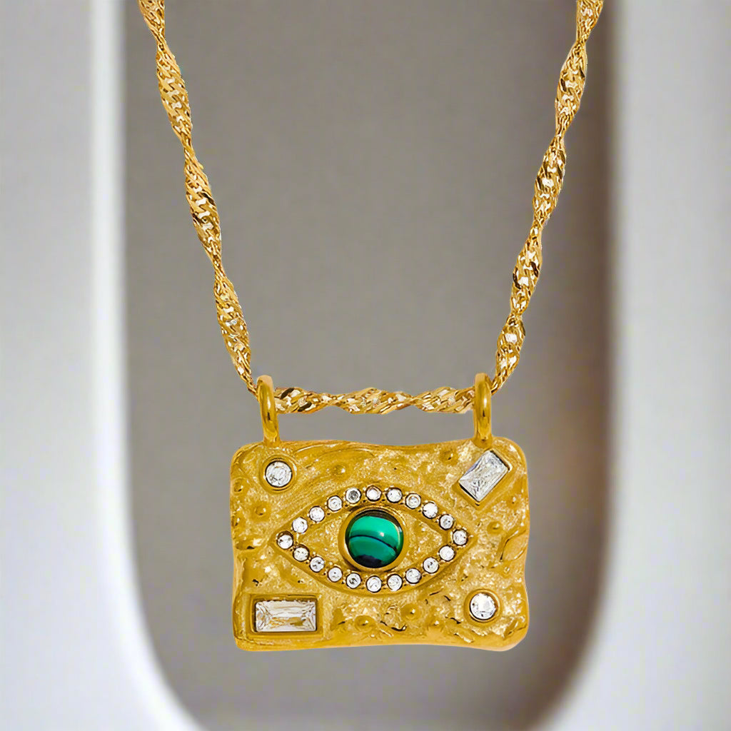 Gold necklace with an eye-shaped pendant featuring a green gemstone on a white background
