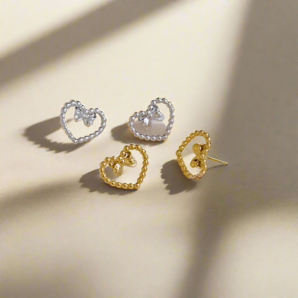 Four heart-shaped earrings in gold and silver on a beige background