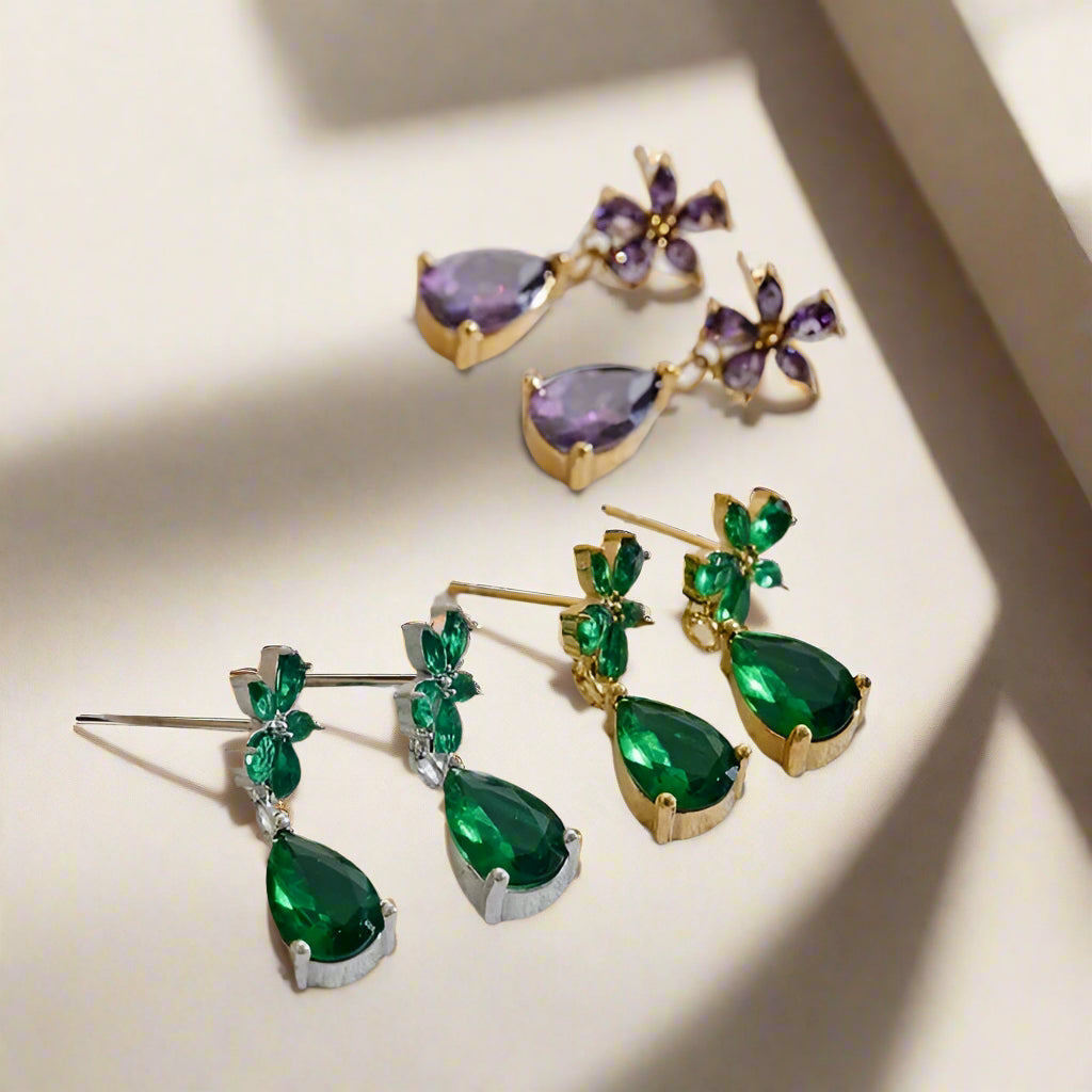 Green teardrop earrings with gold accents on a textured white surface