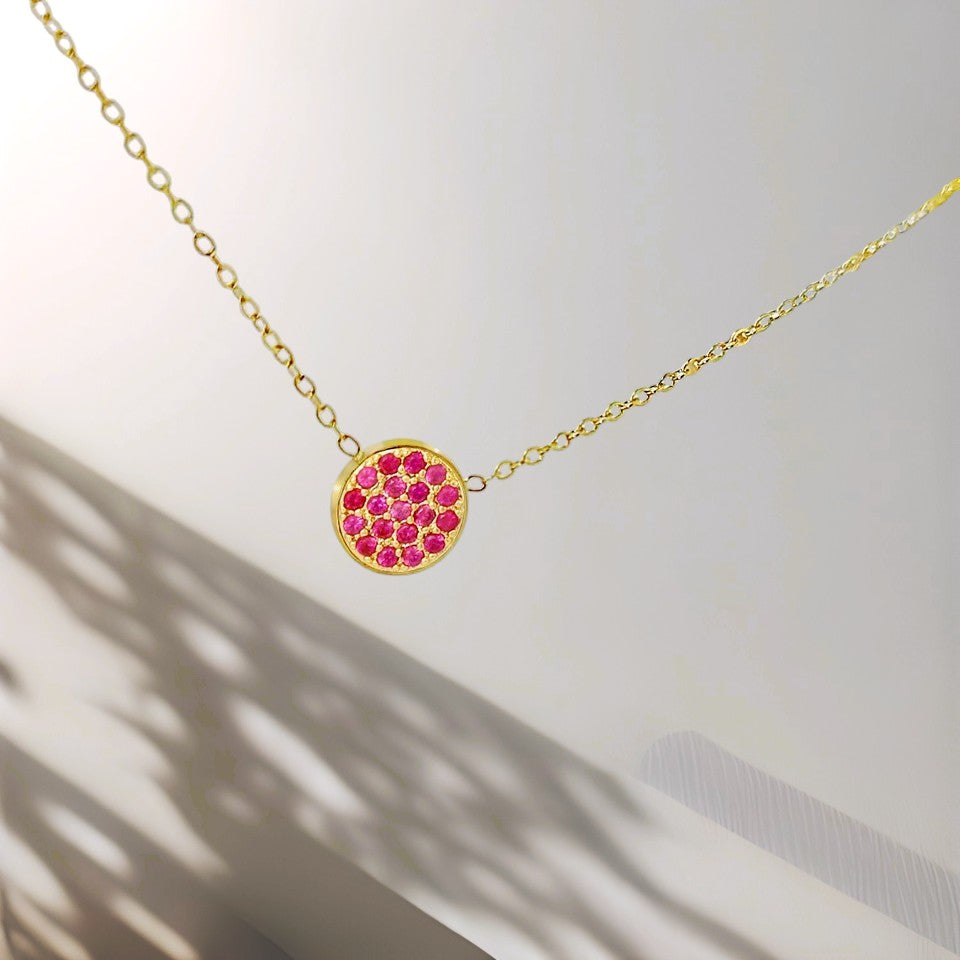 Gold necklace with a pink gemstone pendant on a light background
