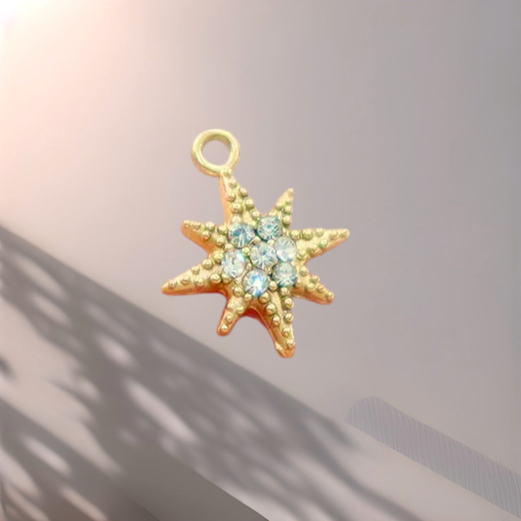 Gold star-shaped pendant with blue stones on a soft pink background