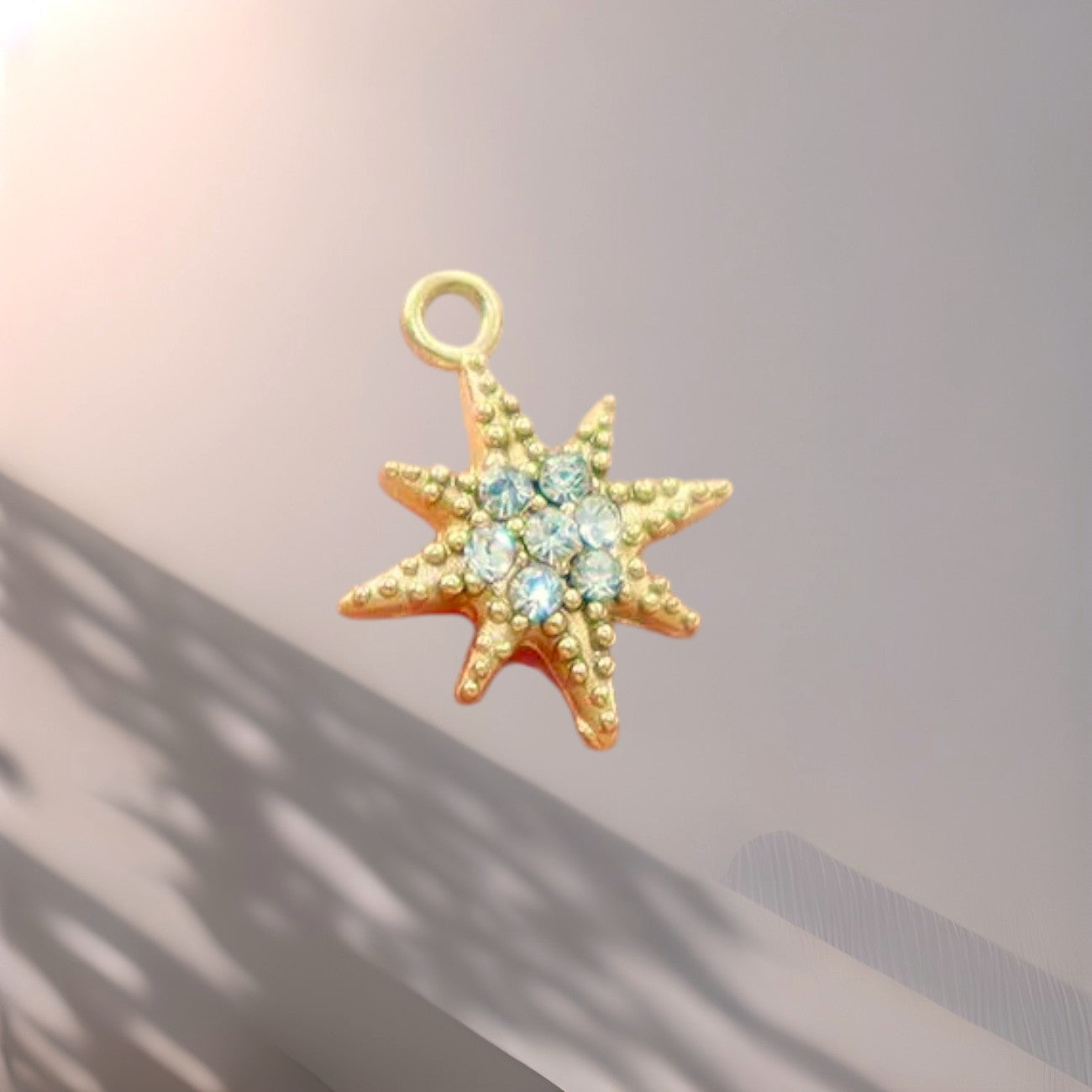 Gold star-shaped pendant with blue stones on a soft pink background