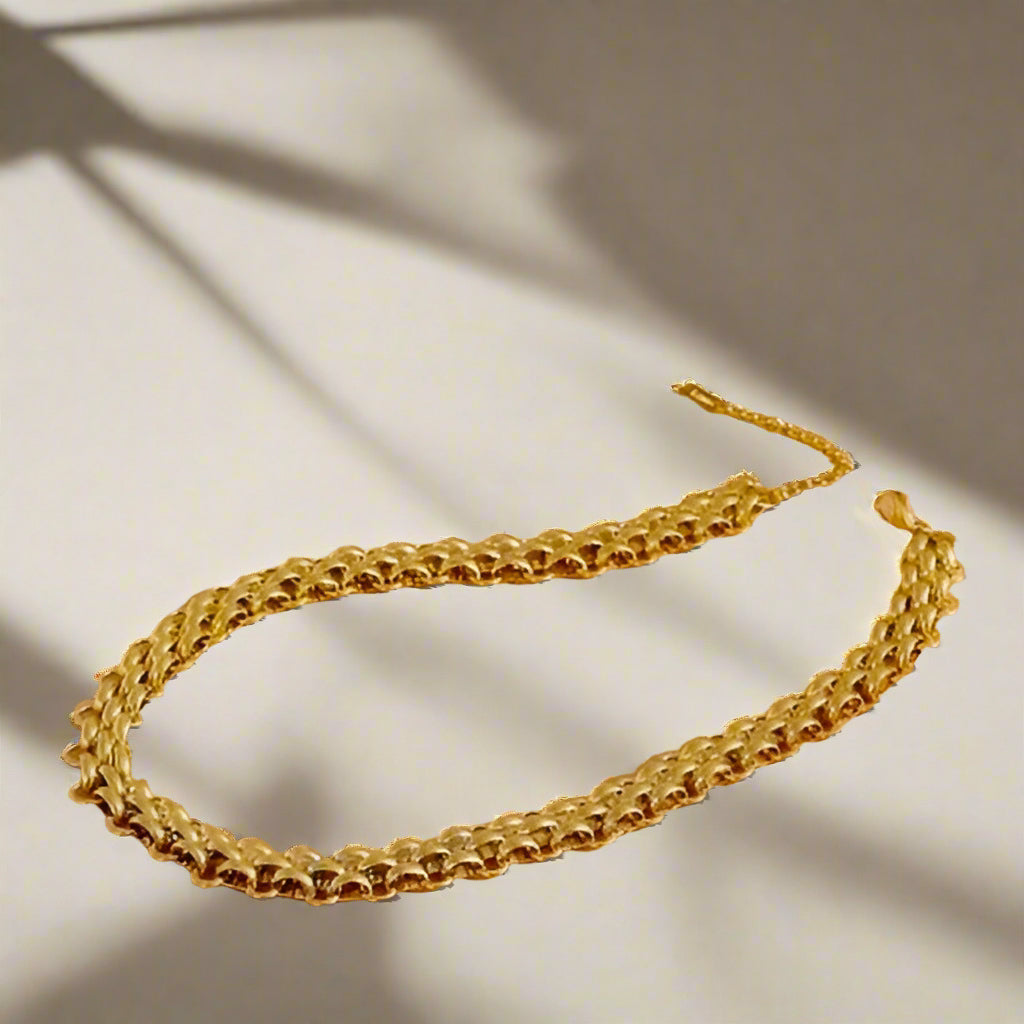 Gold necklace on a textured surface with dried plants and rocks.