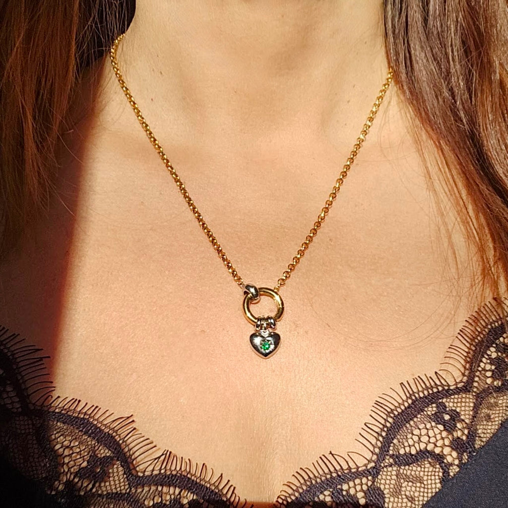 Gold necklace with a heart-shaped pendant featuring green gemstones, worn by a woman.