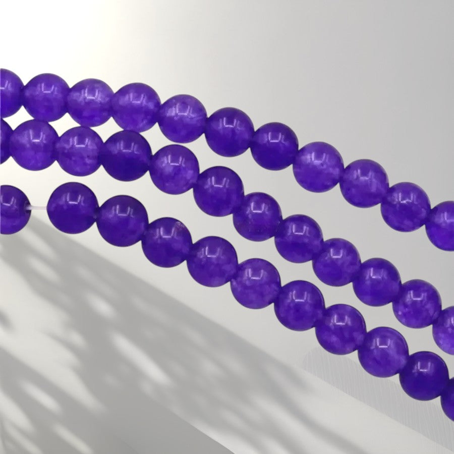 Three strands of polished purple beads, likely amethyst, arranged diagonally on a light gray background with soft shadows.