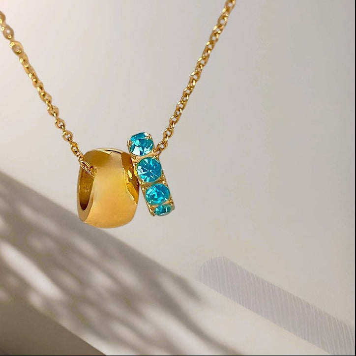 Gold necklace with a blue gemstone pendant on a neutral background